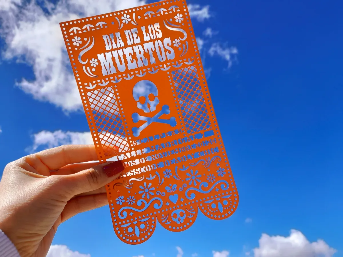 Papel picado naranja con calaveras y flores hecho con troquelado láser